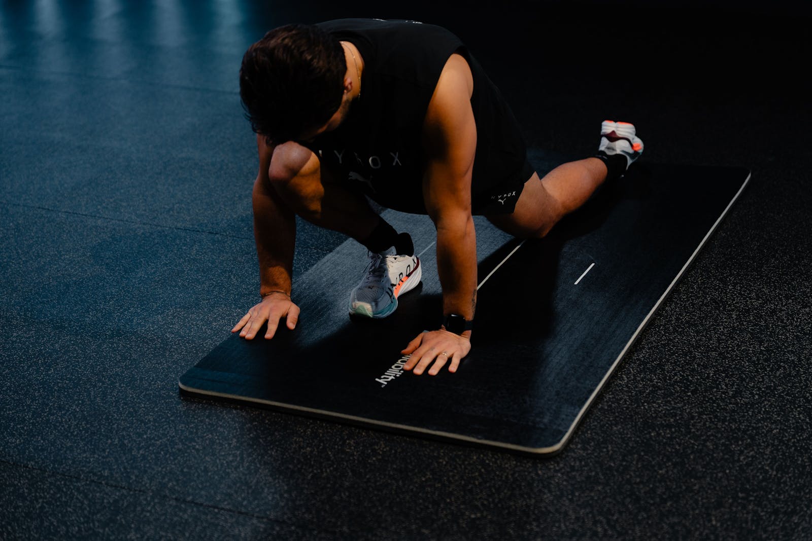Athlete working through a deep lunge hip opener on a mat in a dark gym